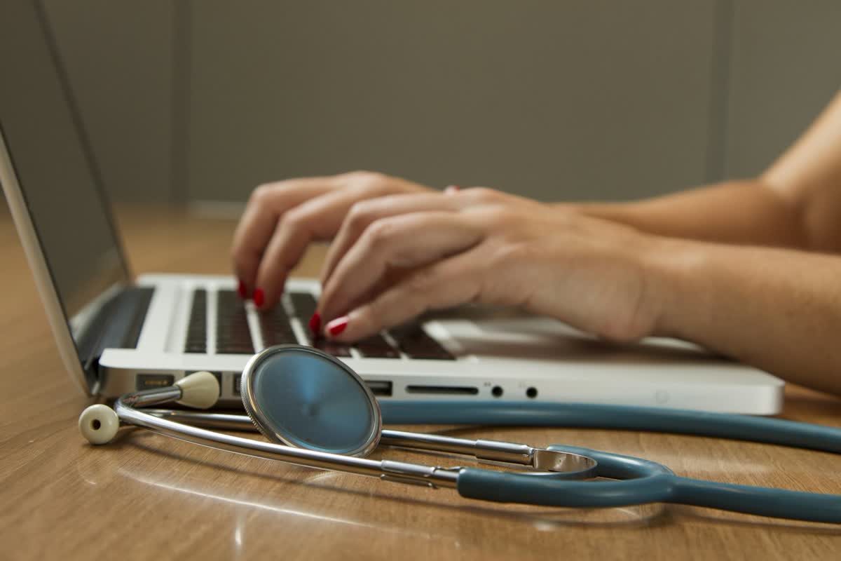 A clinician's hands at a laptop beside a stethoscope